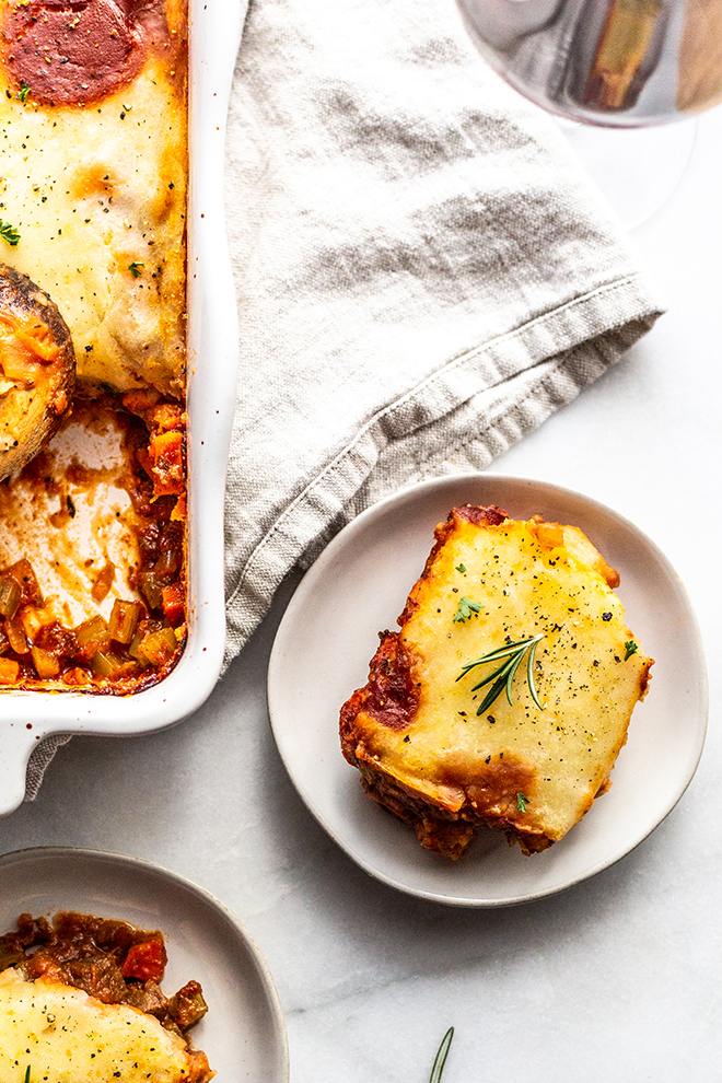 venison shepherd's pie in a pan and on a small plate with a napkin on a white table 