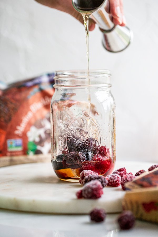 pouring whiskey into a glass jar with berries in it