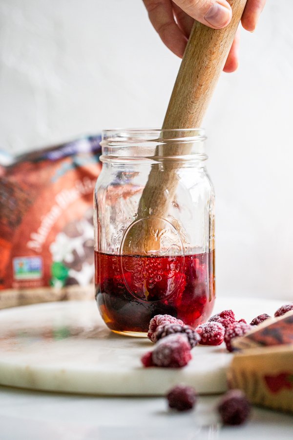 muddling a drink together in a glass jar with berries