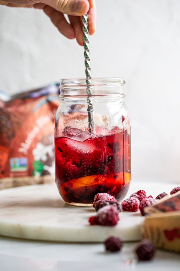 stirring a drink together in a glass jar with berries