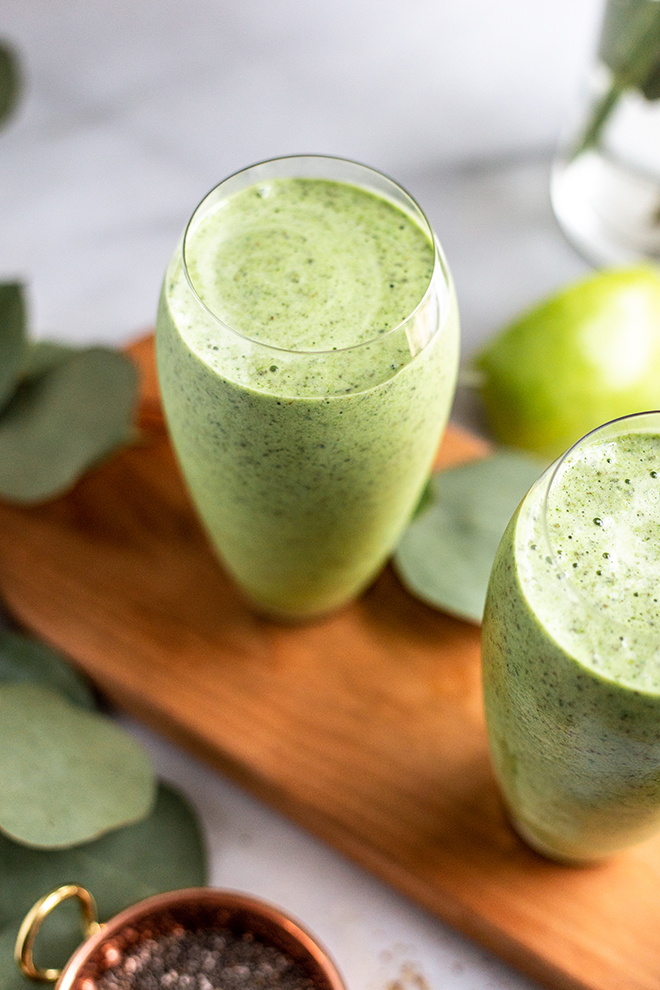 green apple smoothie glasses on a wood board on a white background with leaves and green apple