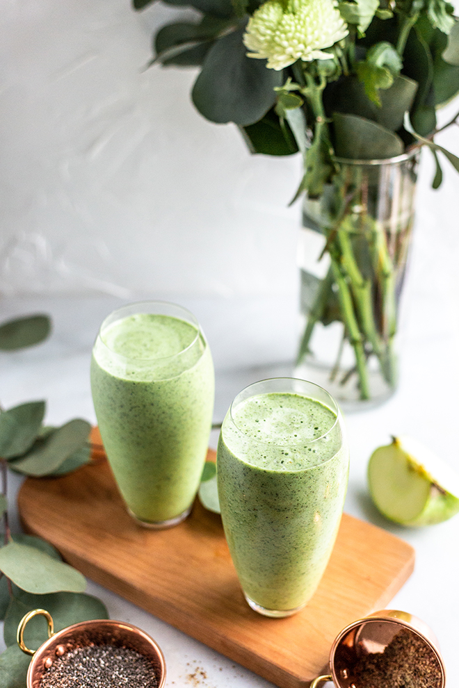 green apple smoothie glasses on a wood board on a white background with leaves and green apple