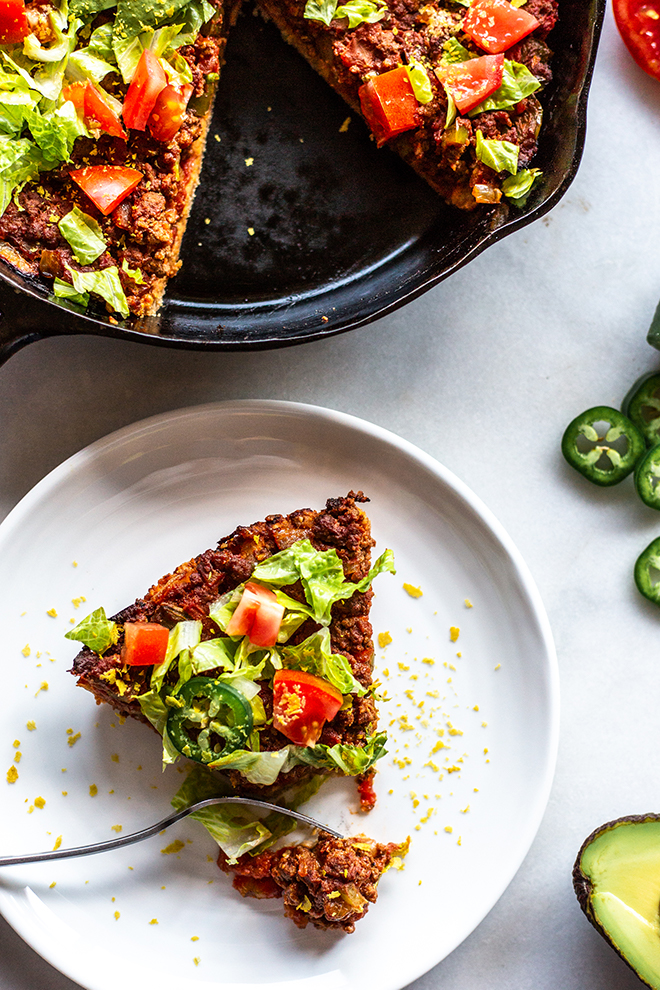 Whole30 Taco Skillet Pie sliced with lettuce, tomato, avocado and hot peppers on a white background. 