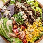 healthy lime greek yogurt dressing over a an elk taco salad in a wood bowl