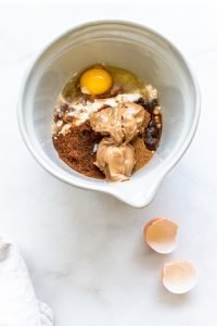 egg, almond flour, coconut flour, coconut oil, coconut sugar, and almond butter in a bowl on a white background
