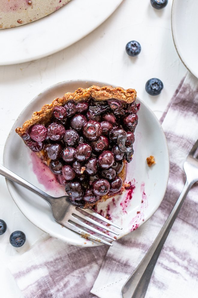 a slice of paleo blueberry tart on a white background