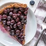 a slice of paleo blueberry tart on a white background