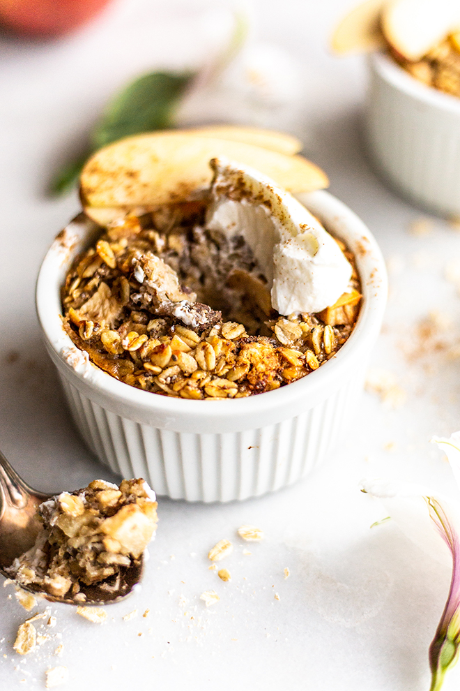 baked apple pie oatmeal topped with Greek yogurt with a bite taken out shot on a white background 