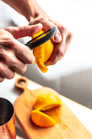 peeling an orange with a grey vegetable peeler