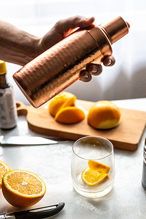 shaking an old fashioned cocktail with bourbon glasses, oranges and a wood cutting board