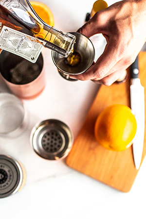 pouring bourbon into a cocktail jigger over a white background, shot from above 