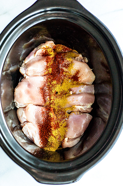 chicken thighs in a black slow cooker with spices 