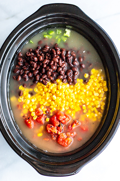 black beans, corn and tomatoes in a black slow cooker filled with broth 