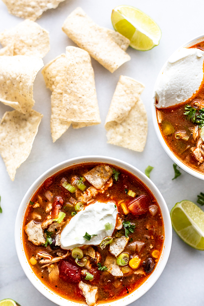 tortilla soup that's red with a dollop of greek yogurt and green onions shot on white marble with chips