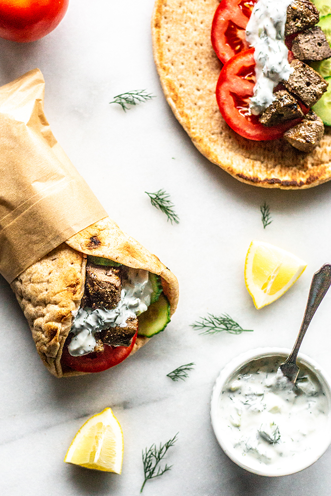 vension gyro on a white background with a bowl of sauce with a pita and a tomato and dill