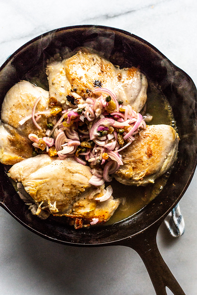 steaming chicken thighs and shallots in a black cast iron skillet