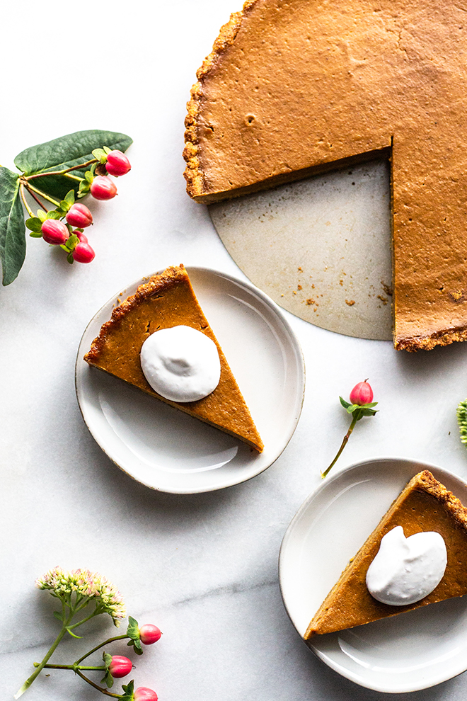 paleo pumpkin tart sliced on plates with whipped cream on a white background and flowers