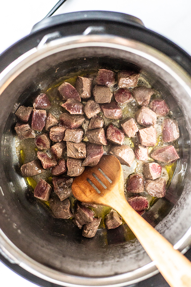 venison sauteed in an instant pot with a wooden spoon 