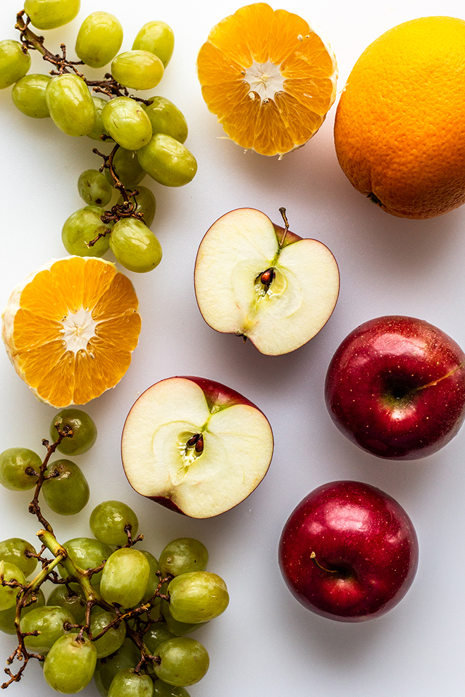 grapes, oranges and apples on a white cutting board