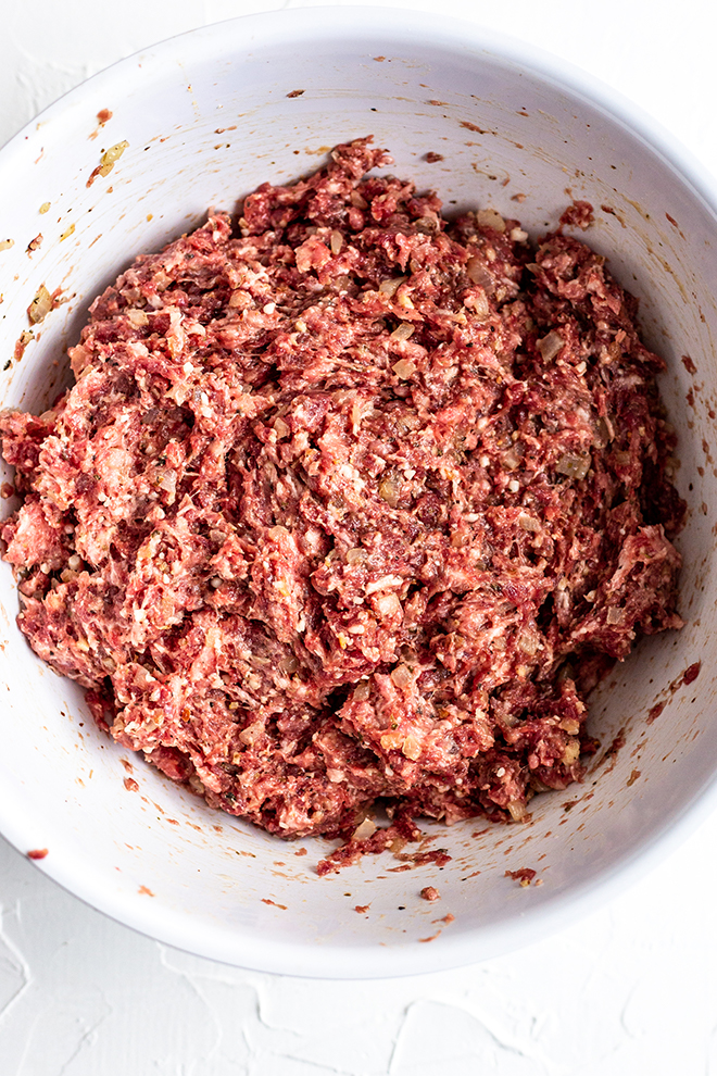 pork and venison meat mixed with aromatics in a white bowl