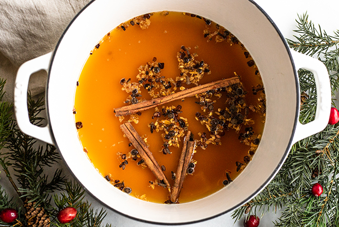 apple cider and mulling spices in a white pot with winter greens 