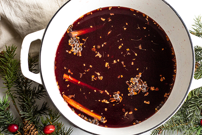 mulled wine with spices in a white pot with greens