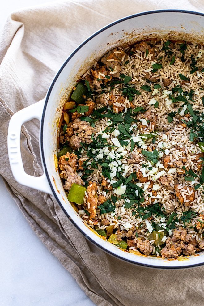 rice, sausage and veggies in a white pot with a cream linen