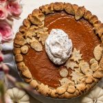 maple bourbon pumpkin pie with pink flowers and whipped cream