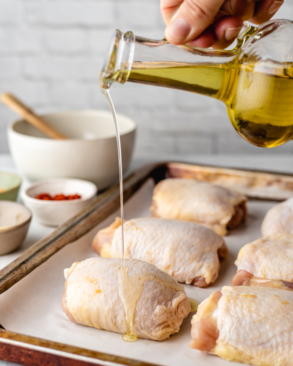 pouring oil on skin-on bone-in chicken thighs