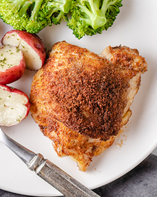 roasted chicken thigh on a plate with potatoes and broccoli