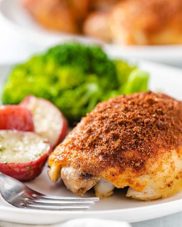 roasted chicken thigh on a plate with potatoes and broccoli