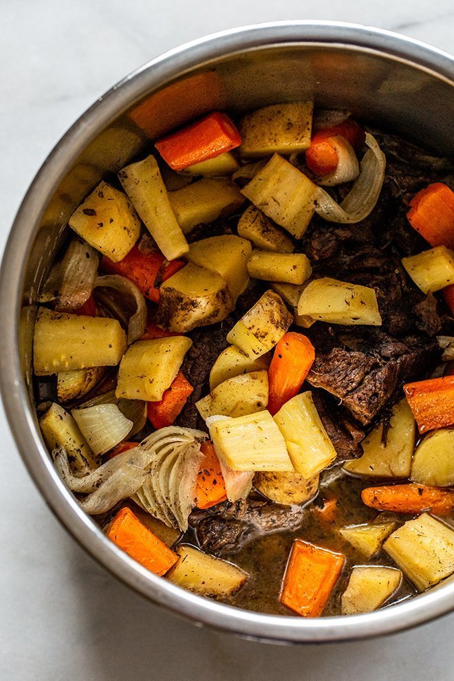 venison seared in the instant pot on a white background with potatoes, parsnips and carrots