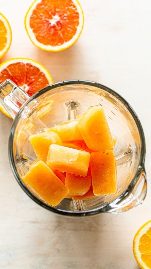 orange ice cubes in a blender with oranges in the background