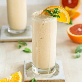 dairy free orange creamsicle milkshake in a slender glass with a coaster on a cream backdrop, mint and oranges
