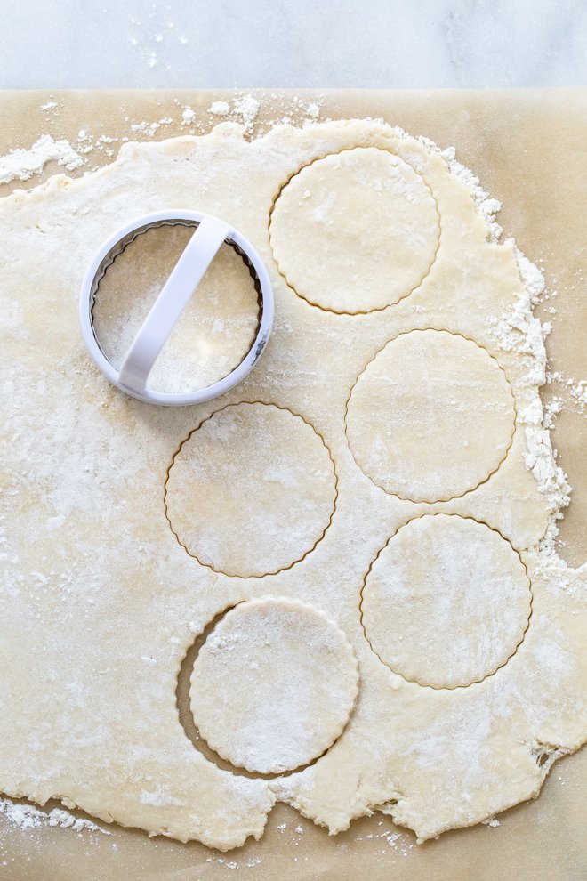 pie dough rolled out on parchment with circles cut out with a biscuit cutter