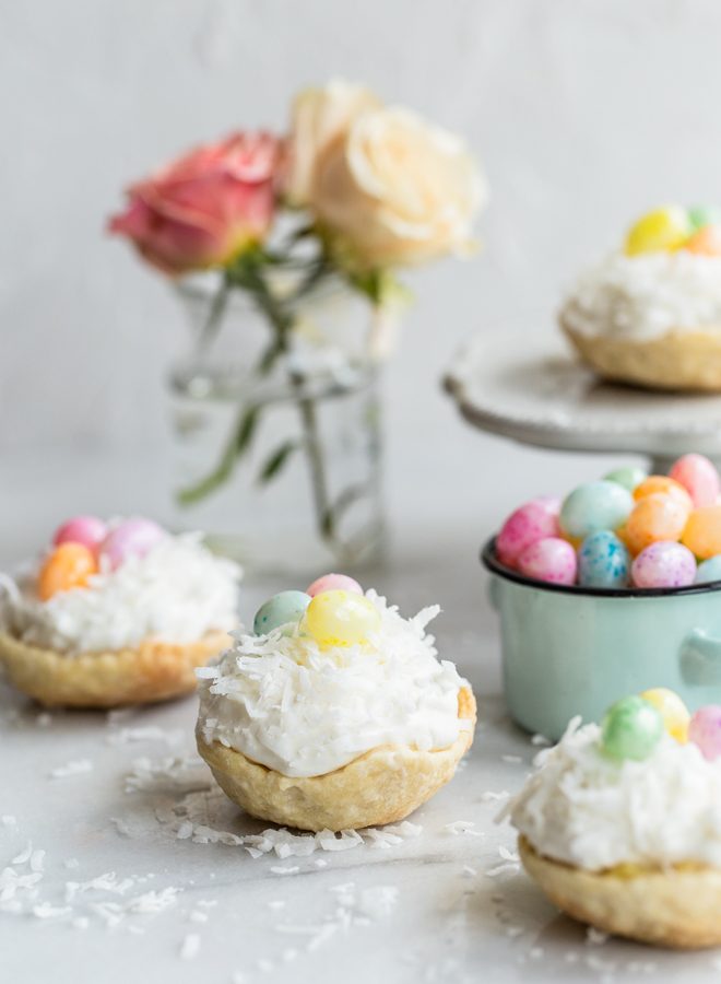 easy mini coconut cream pies with pastel jelly beans on marble with coconut on top and roses and a jelly bean bowl in the background