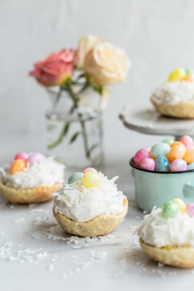 easy mini coconut cream pies with pastel jelly beans on marble with coconut on top and roses and a jelly bean bowl in the background