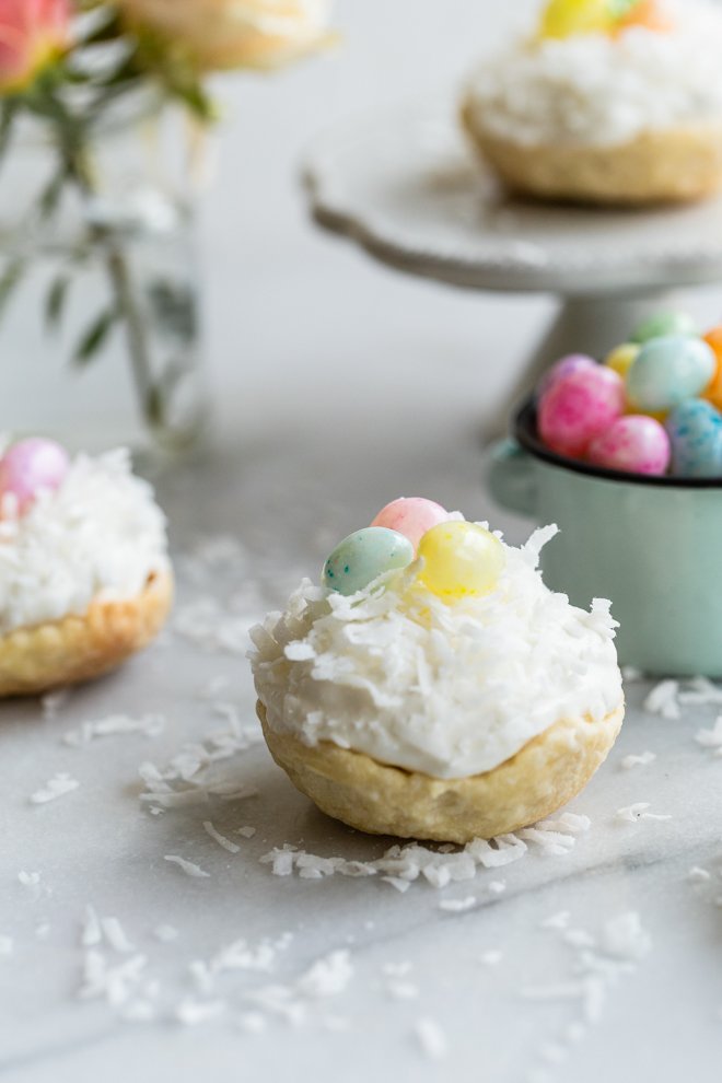 easy mini coconut cream pies with pastel jelly beans on marble with coconut on top and roses and a jelly bean bowl in the background