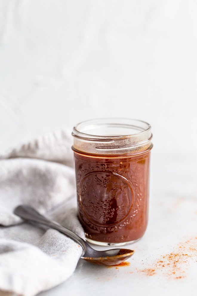 paleo BBQ sauce in a glass jar with a cream linen on a white background with a silver spoon