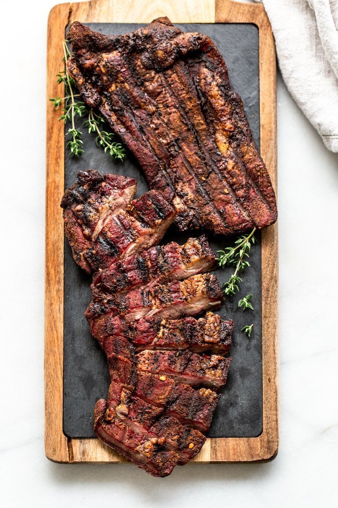 venison brisket on a wood cutting board with slate and thyme