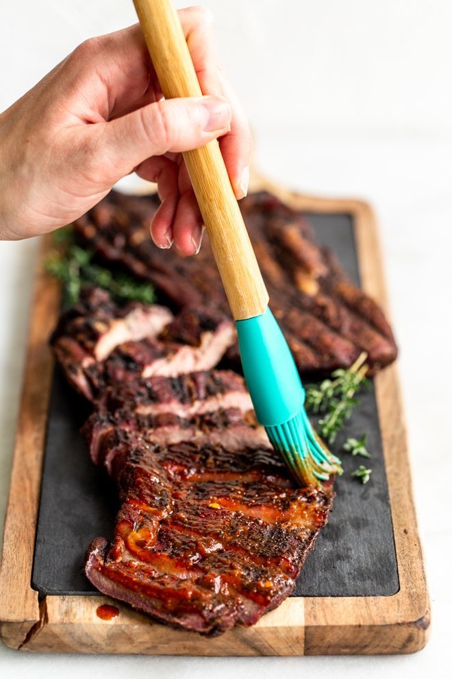 Paleo BBQ sauce being rushed onto brisket sitting on a wood cutting board