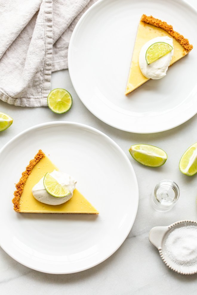 slice of key lime pie on a white plate with a dollop of whipped cream and a lime