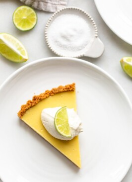 slice of key lime pie on a white plate with a dollop of whipped cream and a lime