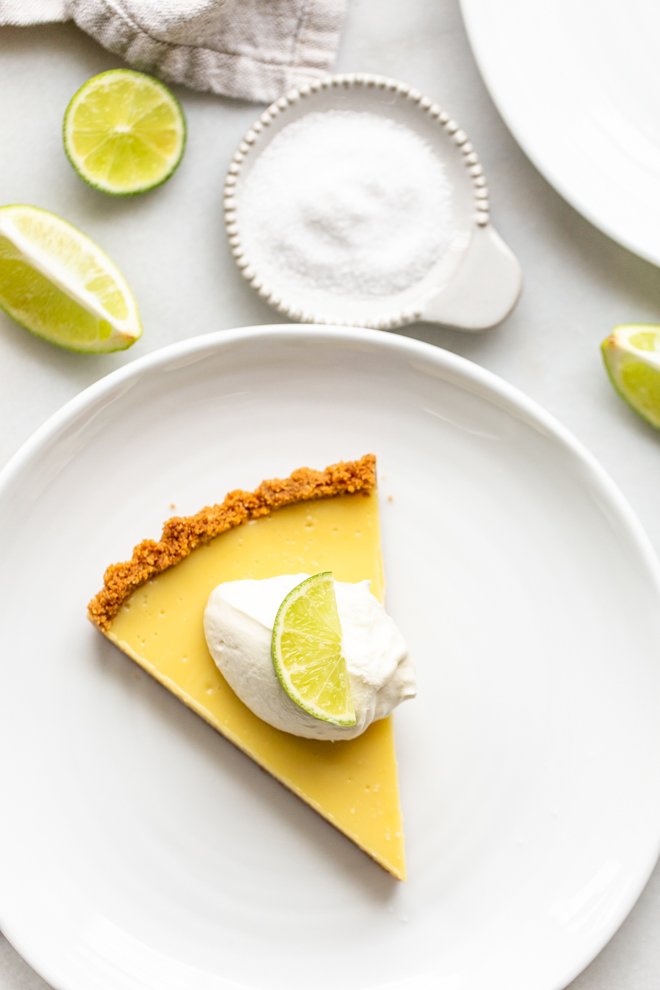 slice of key lime pie on a white plate with a dollop of whipped cream and a lime