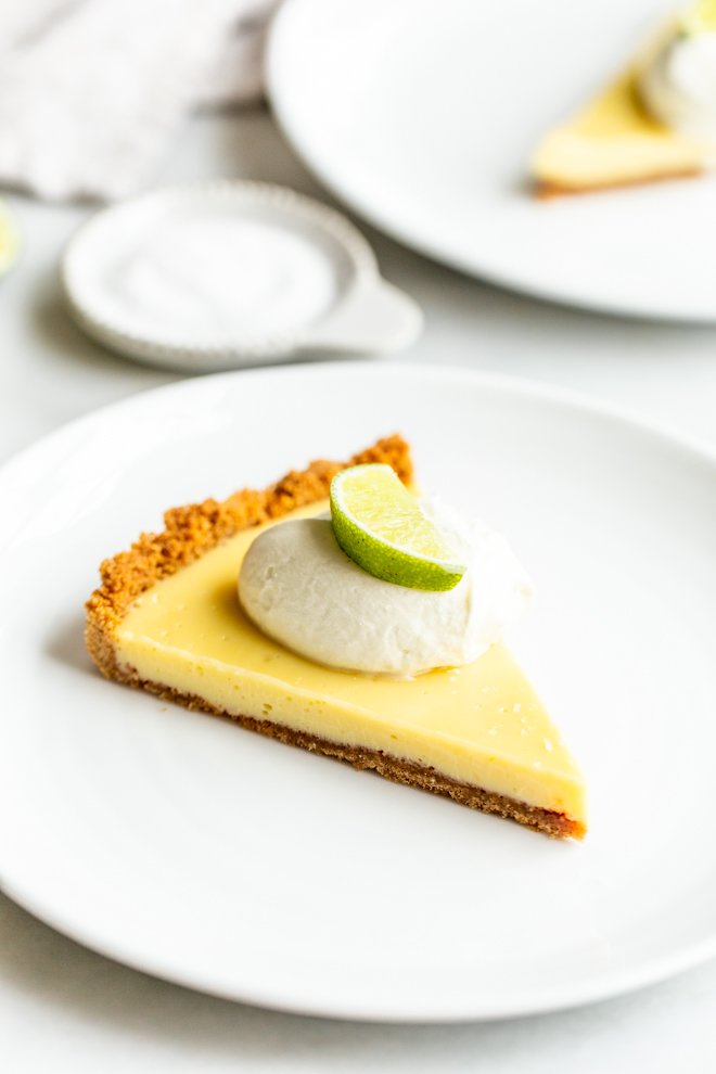 slice of key lime pie on a white plate with a dollop of whipped cream and a lime