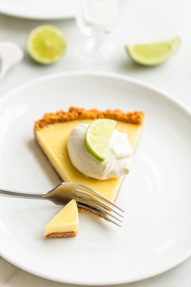 slice of key lime pie on a white plate with a dollop of whipped cream and a lime