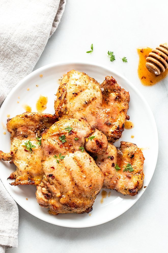 hot honey grilled chicken on a white plate with a white background and a honey covered stirrer 