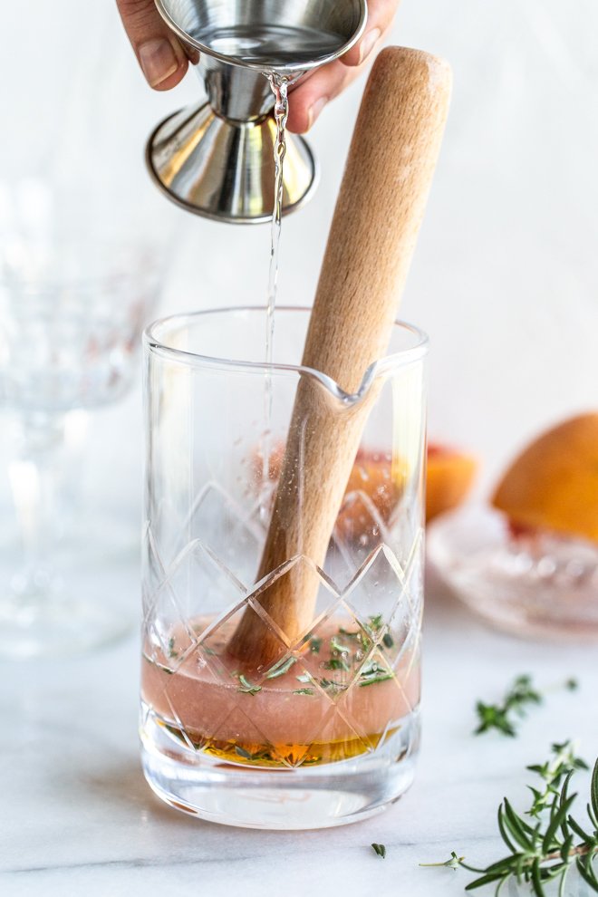 muddling a grapefruit cocktail with a grapefruit slice, a shaker cap, herbs on a white background