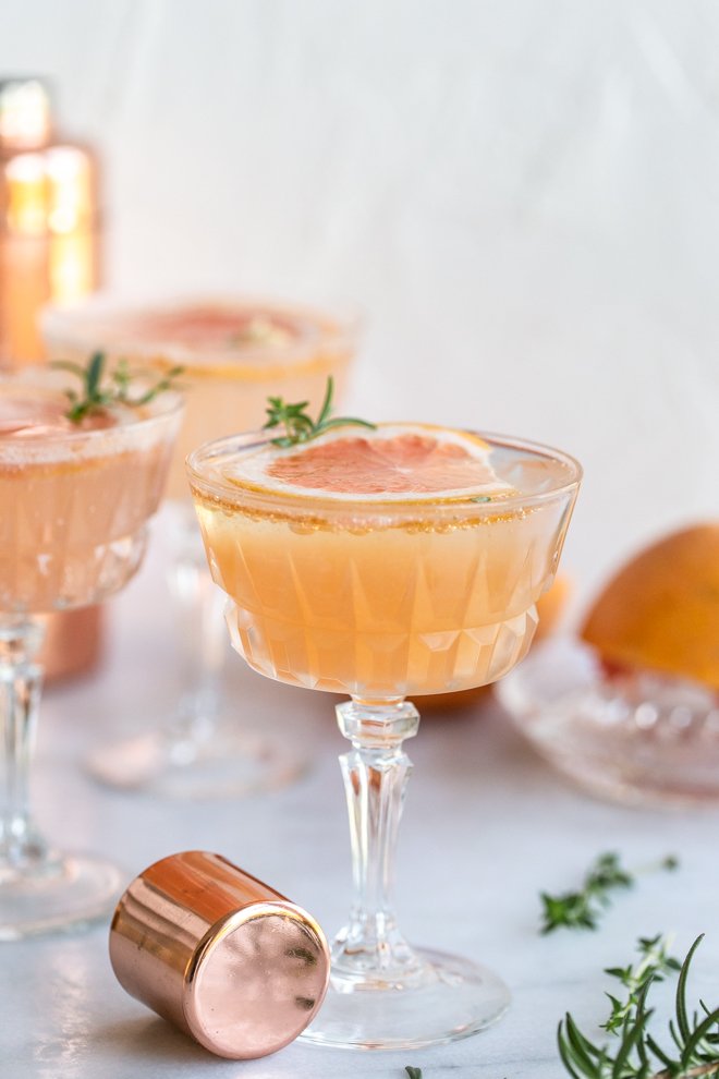 grapefruit cocktail with a grapefruit slice, a shaker cap, herbs on a white background