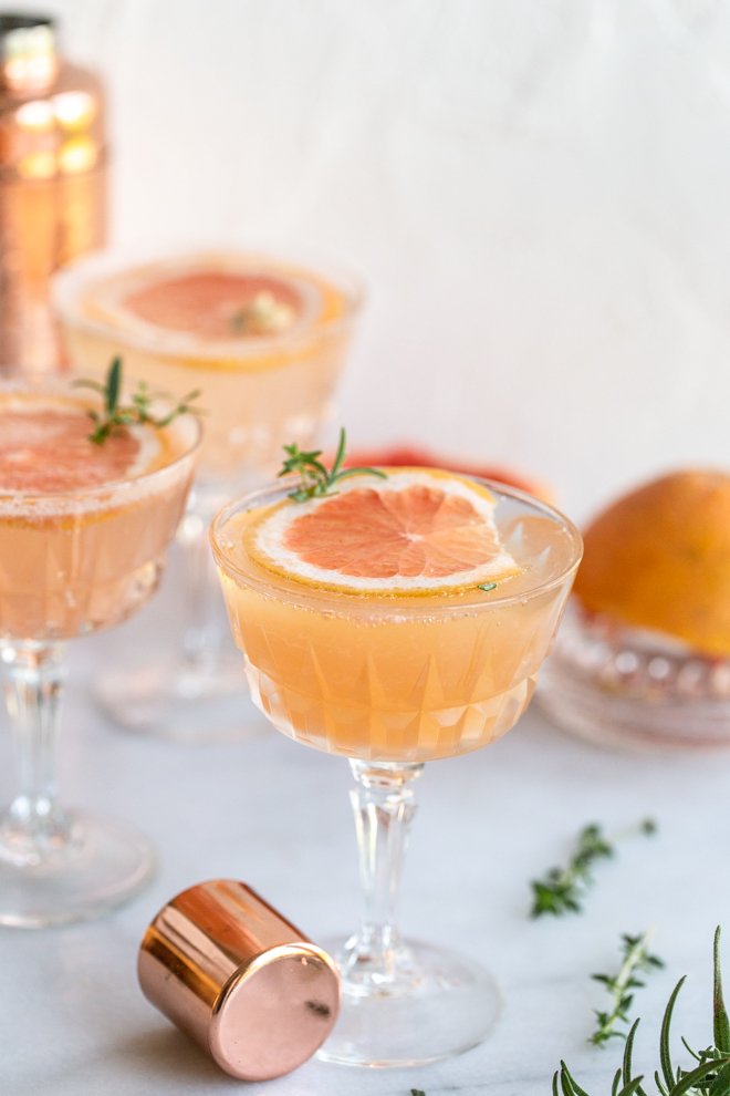 grapefruit cocktail with a grapefruit slice, a shaker cap, herbs on a white background